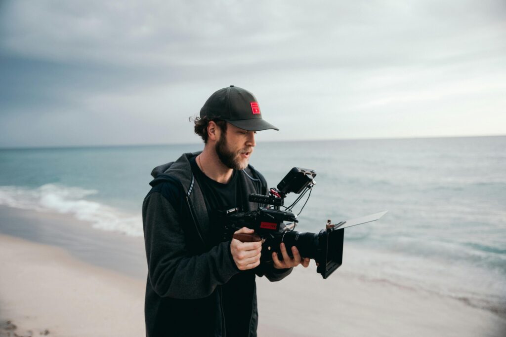 En los medios A videographer with camera gear filming on a beach during sunrise.